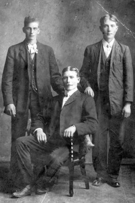 Picture of three men, two standing and one seated in the middle.